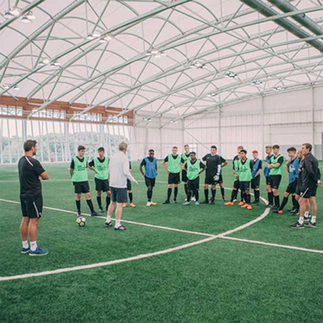 A coach briefs a group of players inside an indoor dome