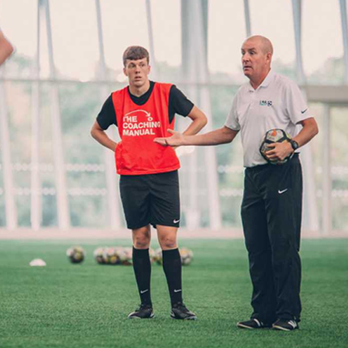 A coach talks one to one with a young player during a session
