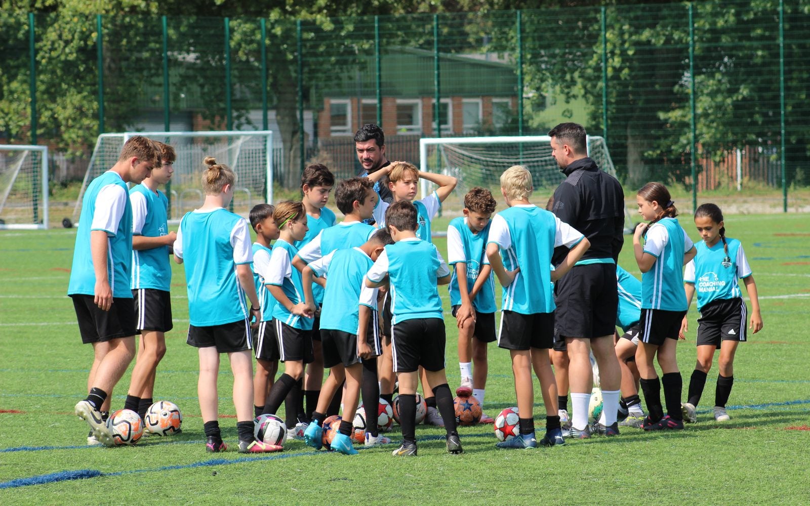 Two coaches talking to a mixed group of young players in The Coaching Manual kit